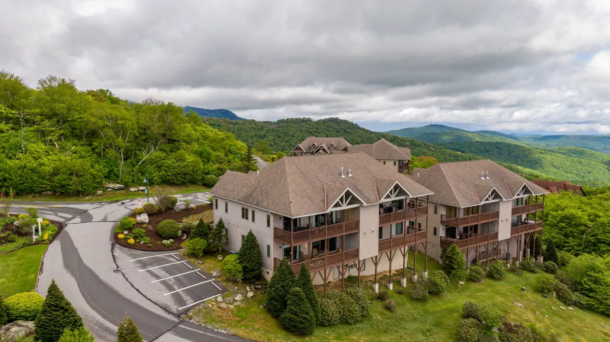 An exterior view of the resort community features landscaped gardens, parking, the building's architecture, and sweeping mountain views in the background. The image subtly hints at community upkeep and the scenic setting.