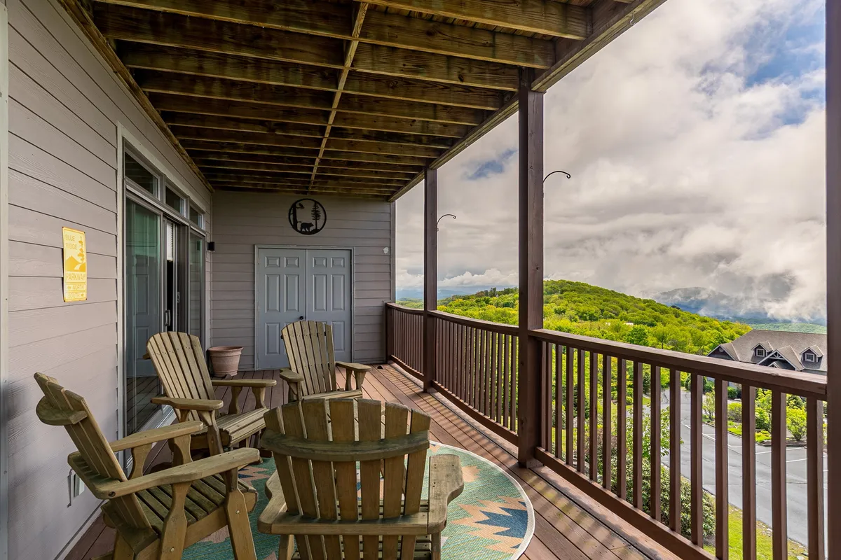 This exterior image features two wooden chairs on a decorative rug positioned to face an expansive mountain view. The doorway to the condo is visible, hinting at easy access from private spaces to the natural surroundings. The mood is peaceful, with soft lighting suggesting either early morning or late afternoon, perfect for intimate moments or quiet reflection.