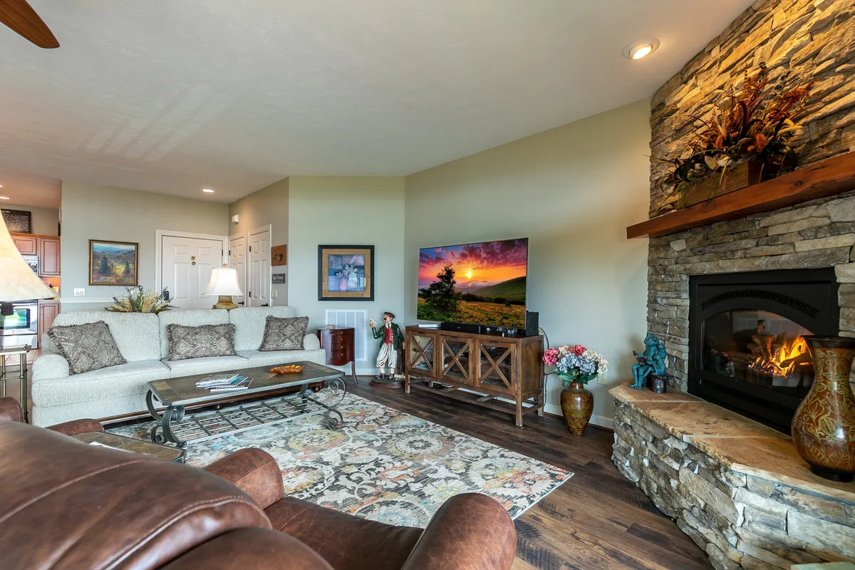 The image displays a warm, inviting living room with a prominent stone fireplace, cozy sofa, television, and a soft rug. The setting is perfect for relaxing evenings and socializing, capturing the essence of resort comfort.