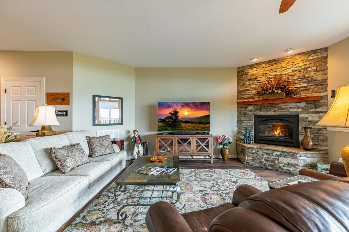 A cozy living area featuring a comfortable sofa, a striking stone fireplace, and a television displaying a scenic landscape image. Decorative accents add warmth, and there’s ample space for gatherings and relaxation.