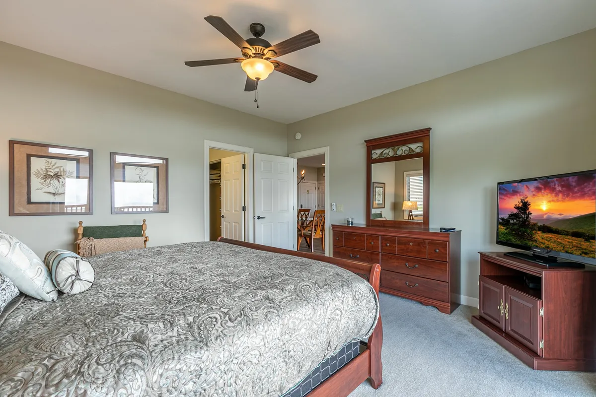 A cozy second bedroom furnished with a comfortable bed, a dresser, ceiling fan, TV, and framed art on the wall. Sunlight filters in, creating a restful space ideal for watching TV or peaceful sleep.