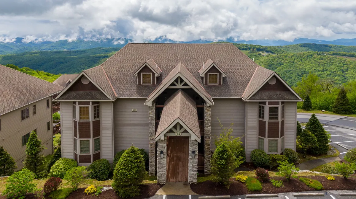 This exterior shot displays the architectural features of the condo building nestled in lush greenery, with the majestic mountains rising in the background. The inviting patio area suggests opportunities for outdoor relaxation and nature appreciation.